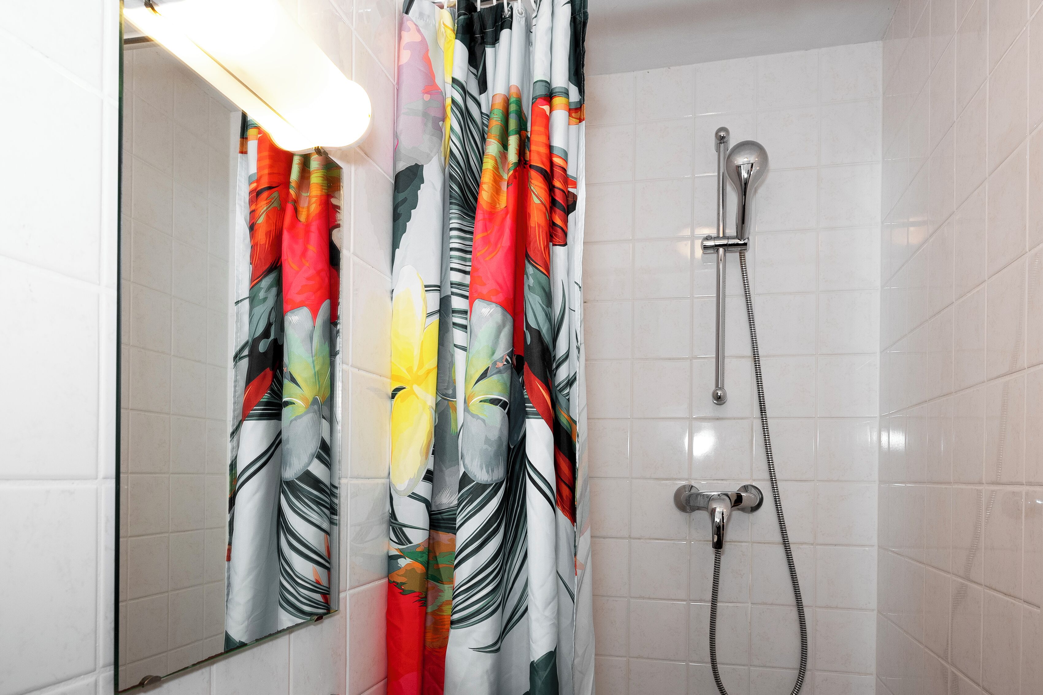 A bathroom with a shower, a mirror, and a tiled wall.