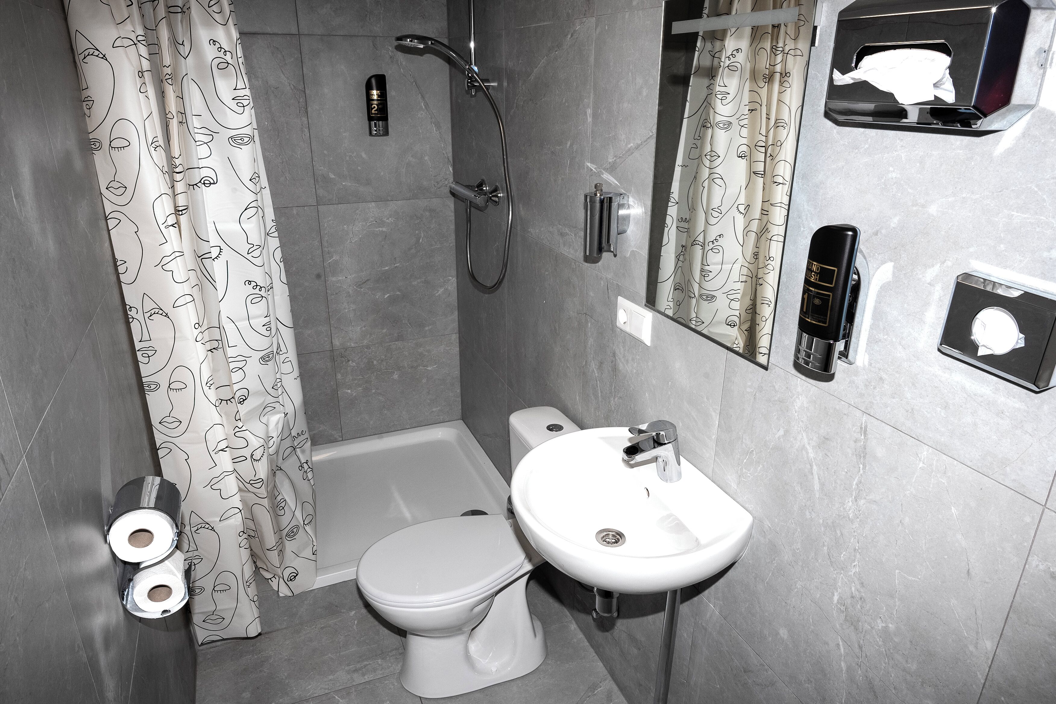 A bathroom with a toilet, sink, shower, and a mirror.