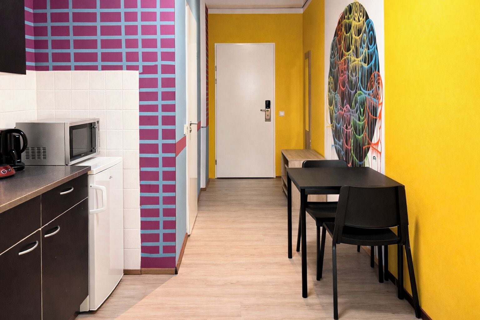 A compact kitchen with a microwave, coffee maker, and cabinets. A dining area with a table and chairs is adjacent to the kitchen.
