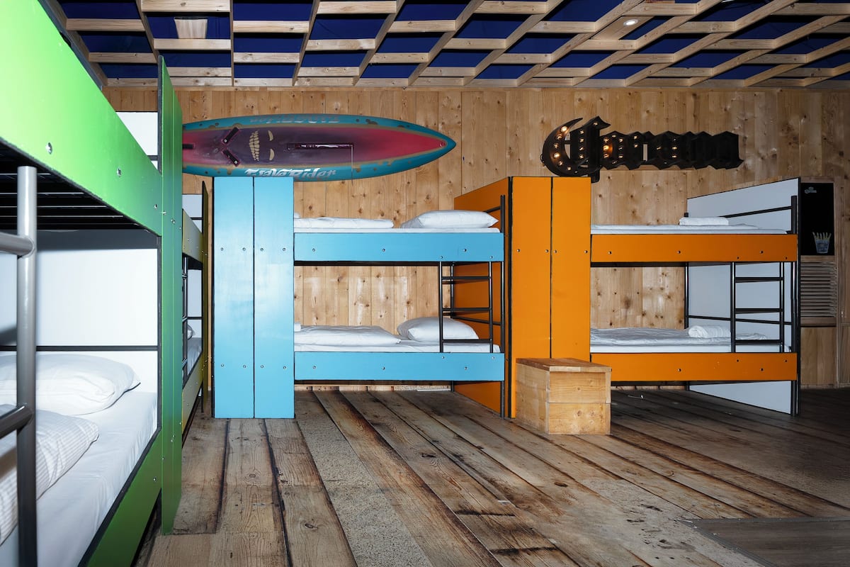 A bunk bed room with a surfboard, wooden walls, and a ceiling with a grid pattern.