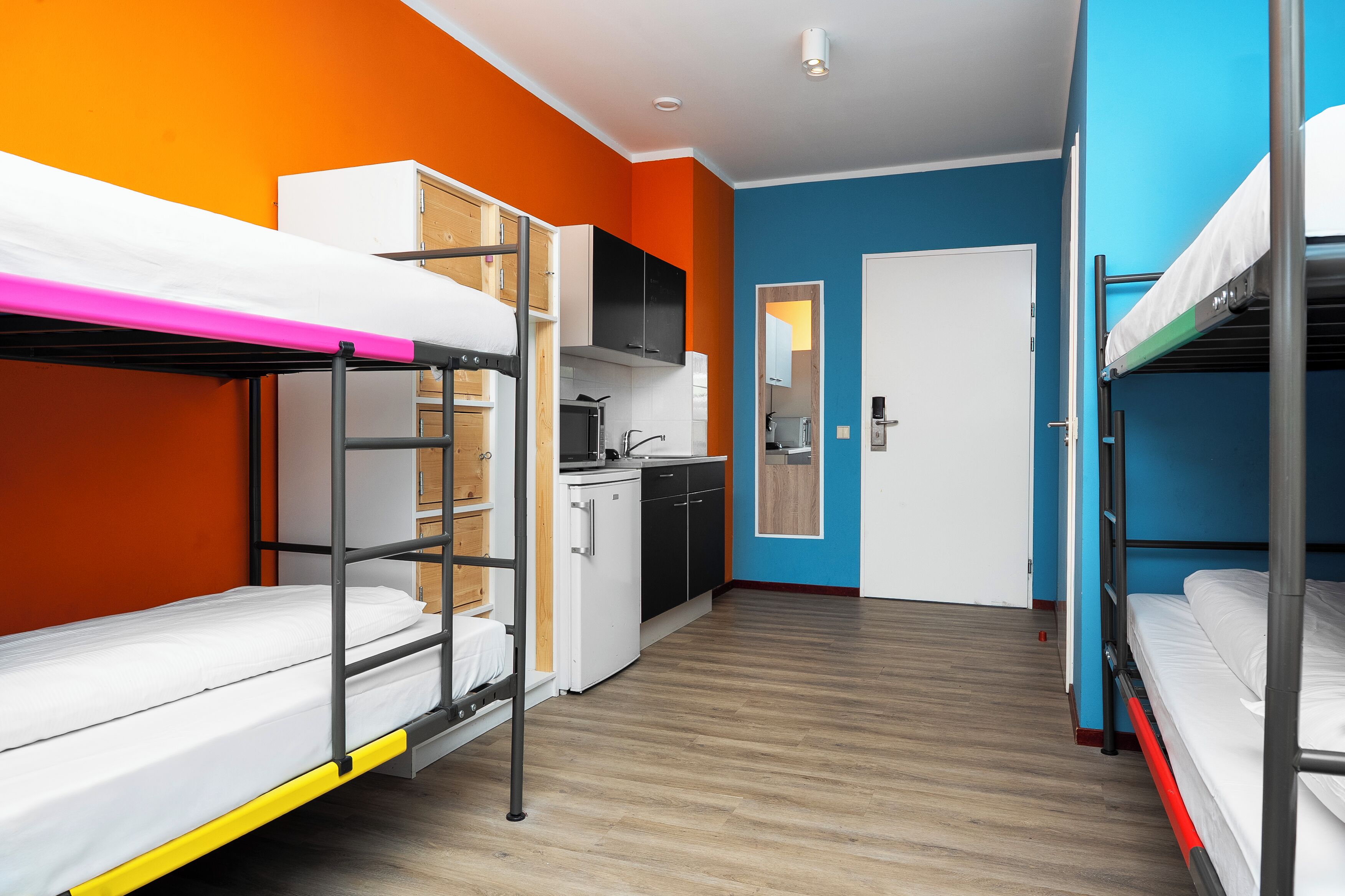 A dormitory room with bunk beds, a kitchenette, and a bathroom.