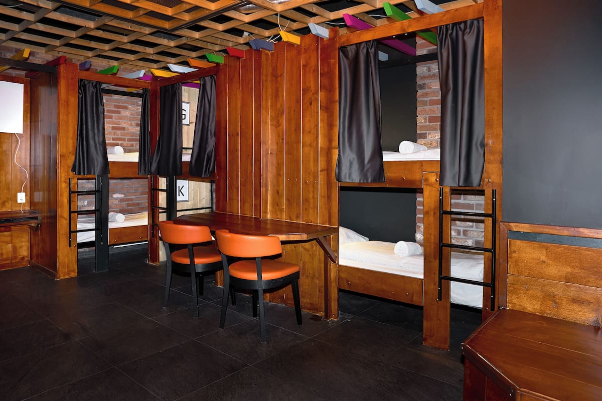 A cozy room with wooden bunk beds, a small table with chairs, and a brick wall.