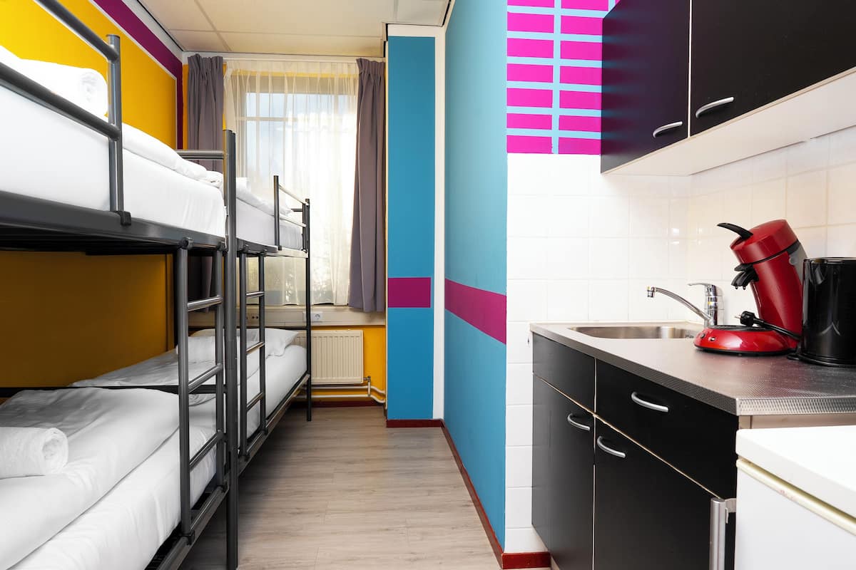 A compact hotel room with bunk beds, a kitchenette, and a window with curtains.