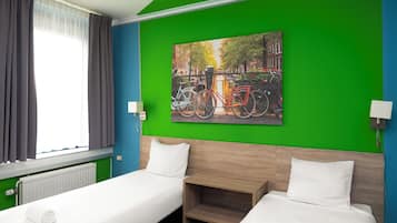 Habitación de hotel con dos camas, pared verde, un cuadro de bicicletas y una ventana con cortinas.