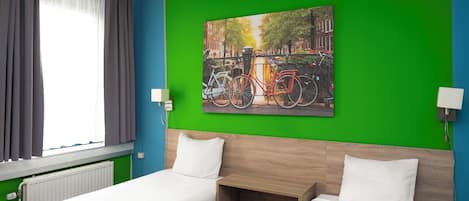 Habitación de hotel con dos camas, pared verde, un cuadro de bicicletas y una ventana con cortinas.