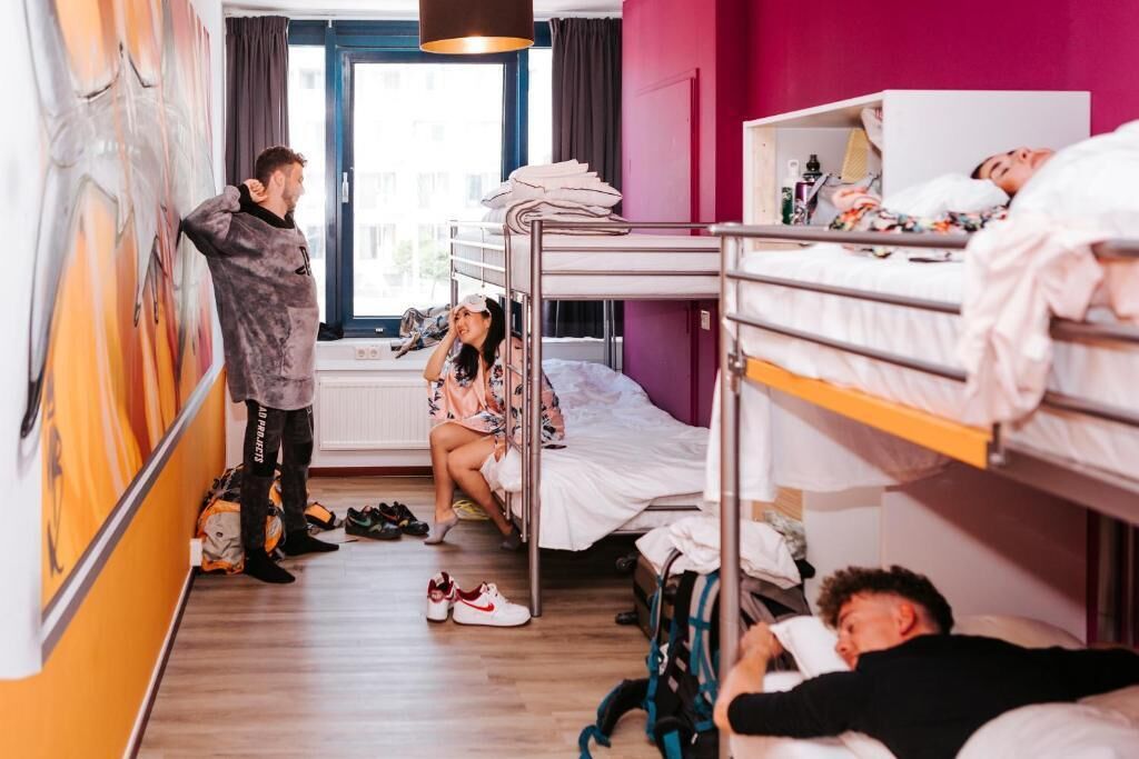 A dormitory room with bunk beds, a window with curtains, and a radiator.