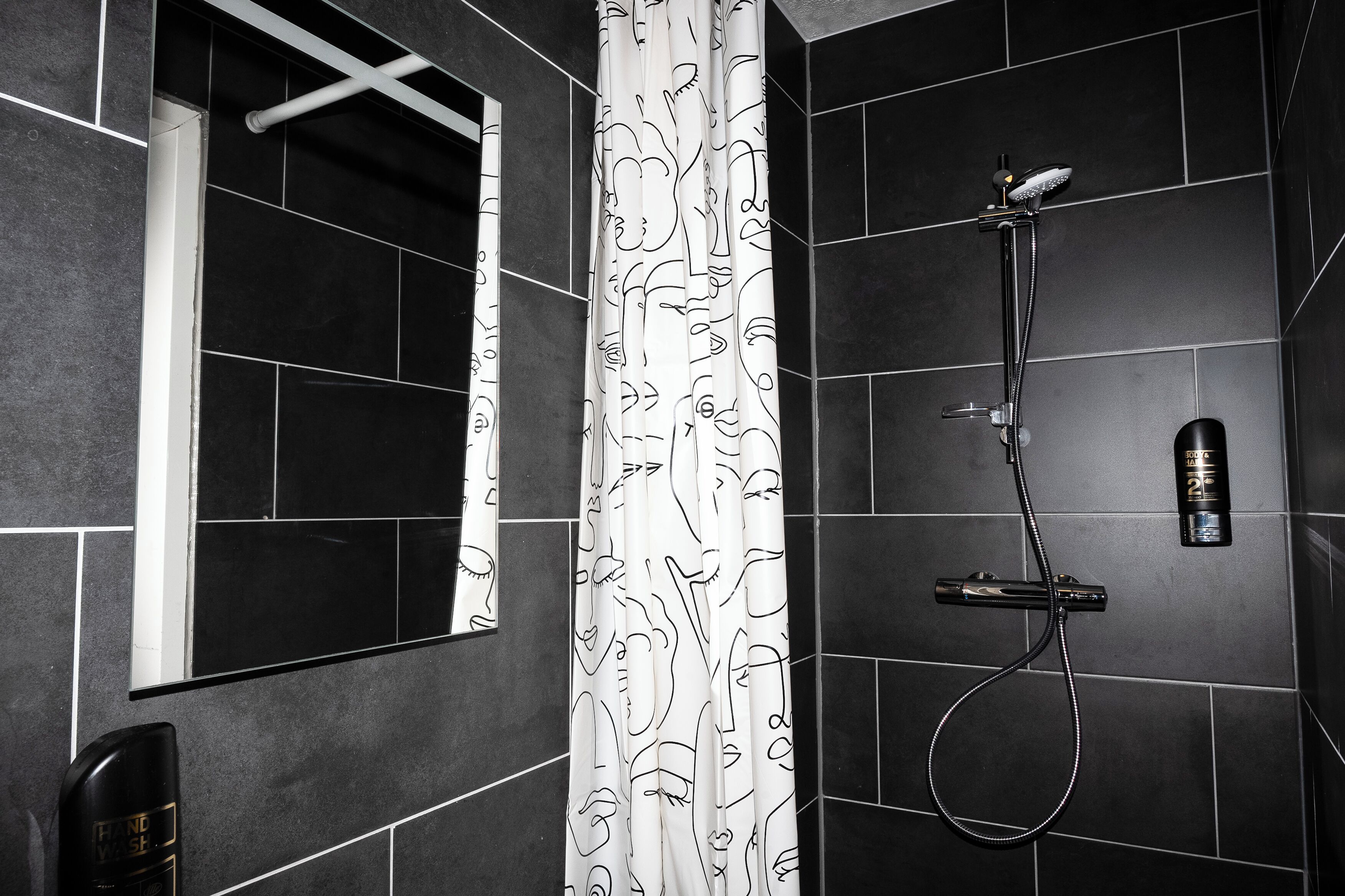 A modern bathroom with dark tiles, a shower with a handheld showerhead, and a toilet with a hand dryer.