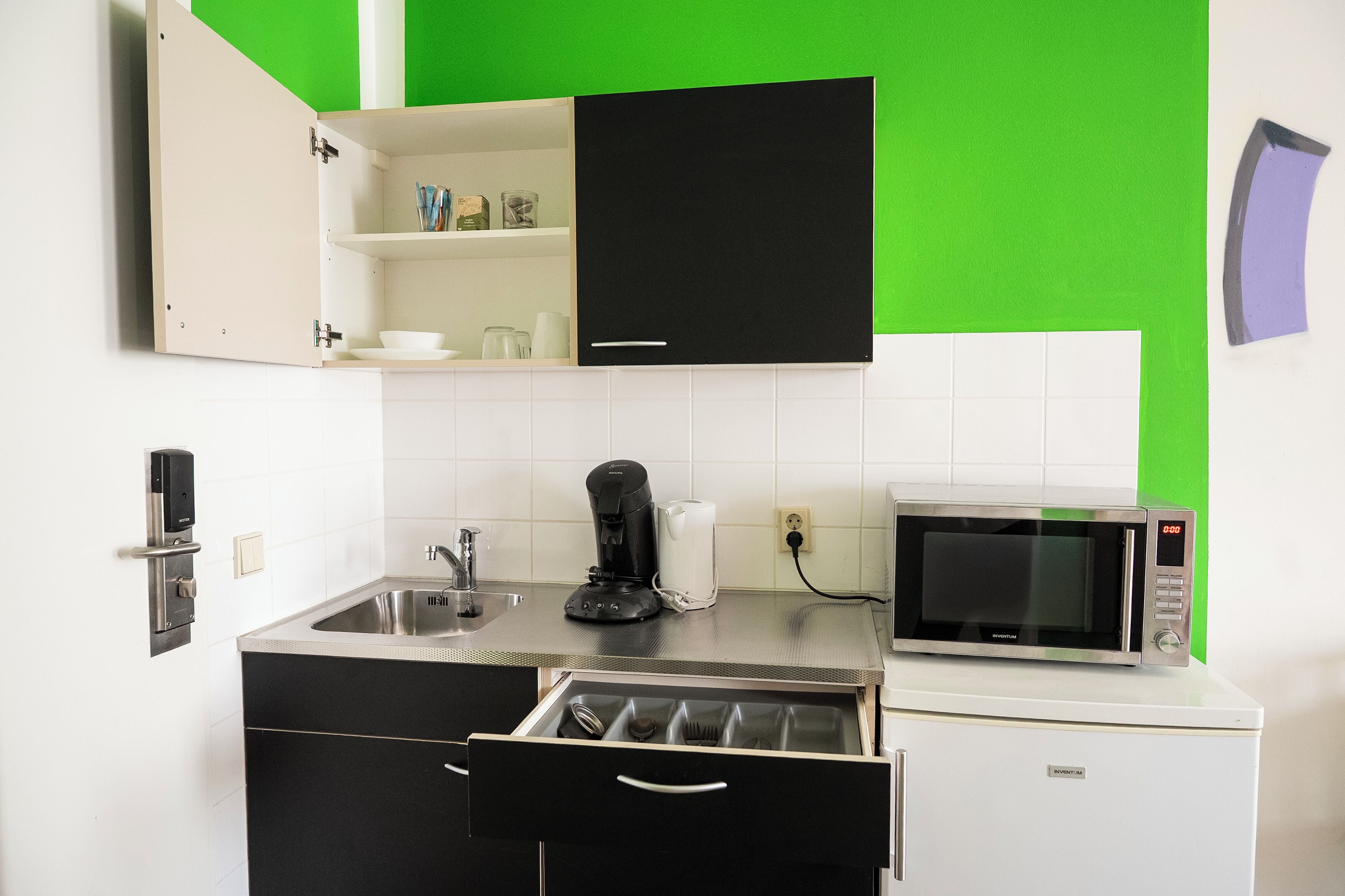 A compact kitchen with a microwave, coffee maker, and a drawer with utensils.