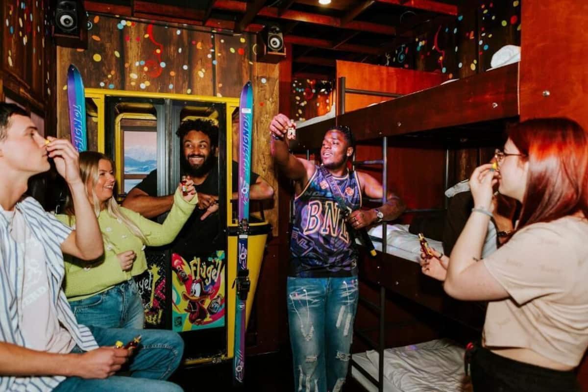 A group of people in a room with bunk beds and a colorful poster on the wall.