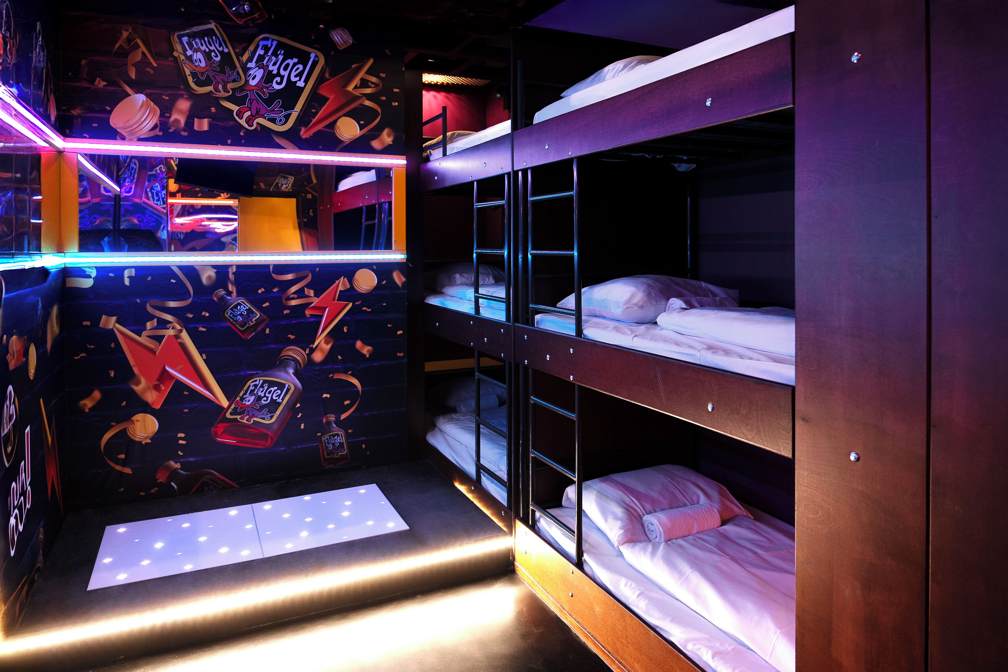 Ein Schlafraum mit Etagenbetten, einer Neonreklame und einem kleinen Tisch.