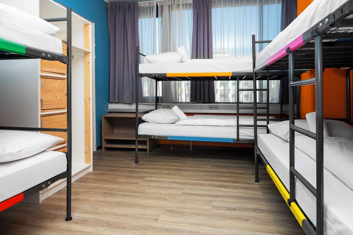 A bunk bed room with a wooden floor, a window with curtains, and a desk.