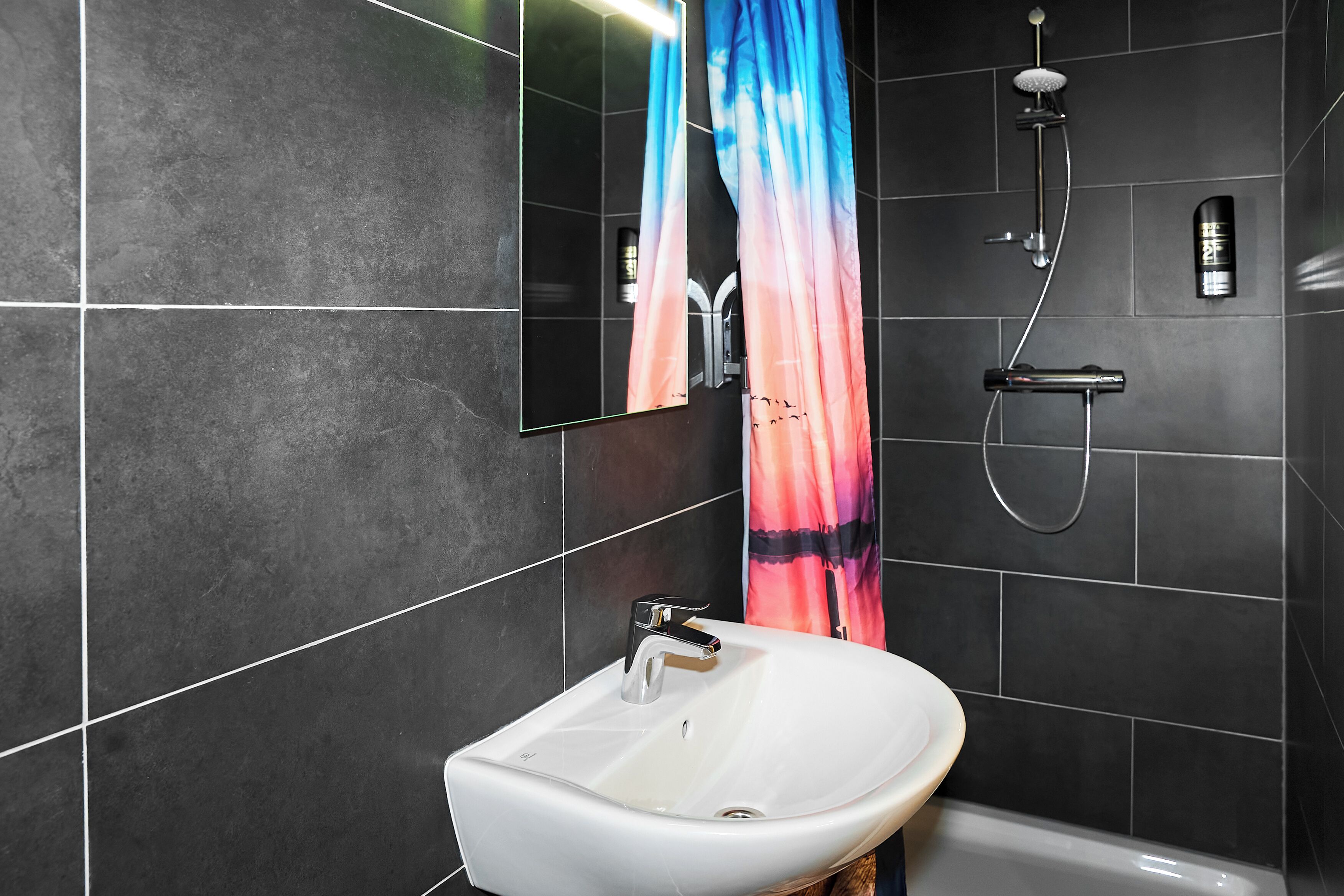 Ein Badezimmer mit einem weißen Waschbecken, einem Spiegel, einer Dusche inklusive Duschbrause und einem Handtuchhalter.