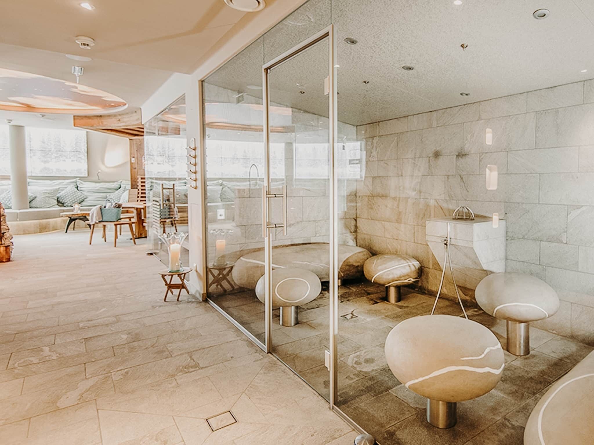 A modern spa with a glass wall, a seating area with a sofa and chairs, and a stone floor.