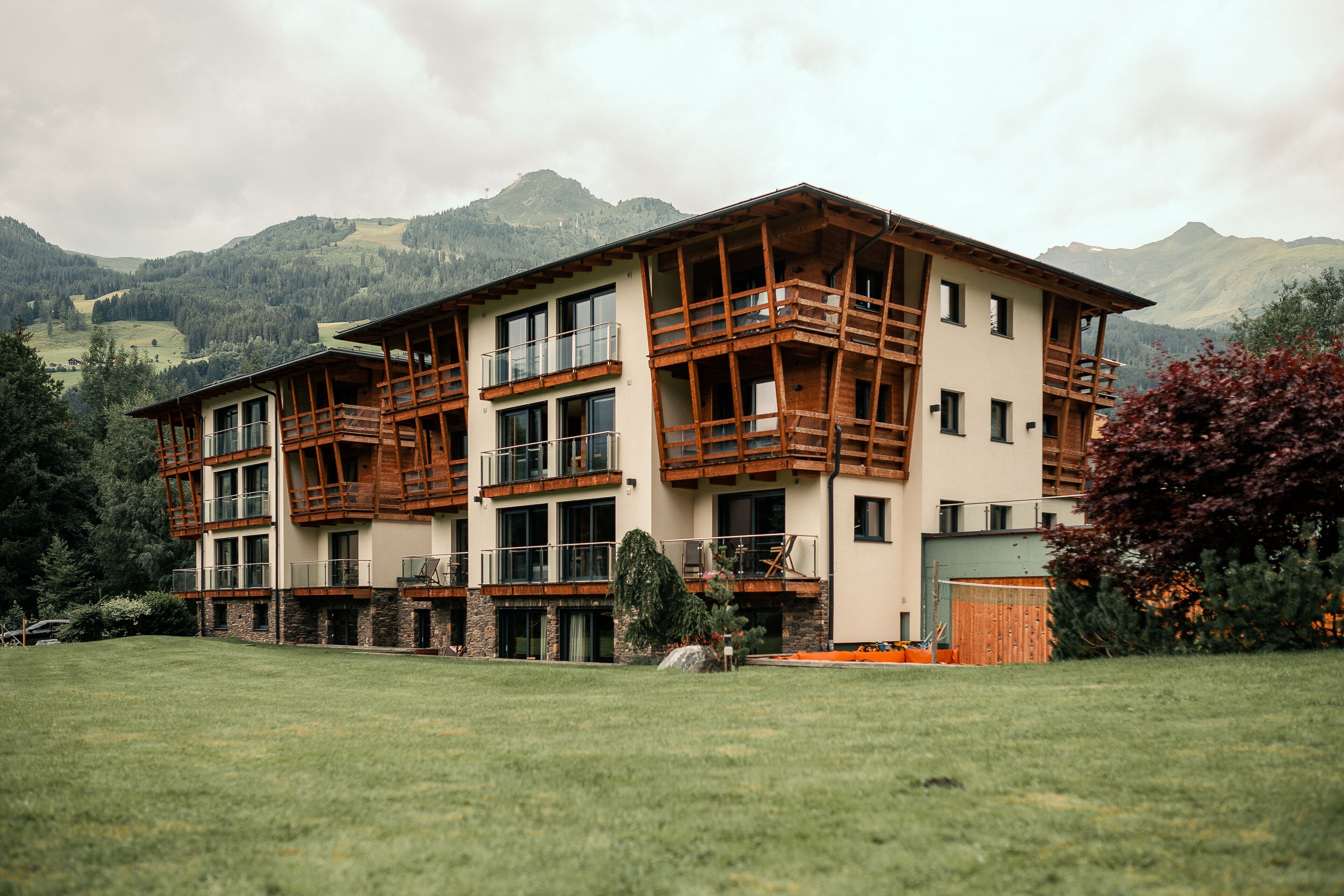 A multi-story building with wooden balconies, large windows, and a view of mountains in the background.