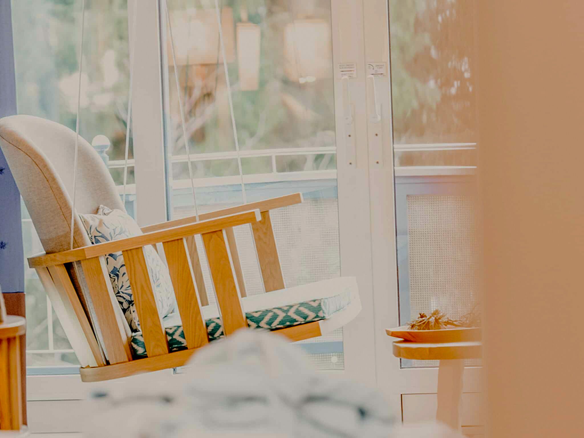 A chair with a wooden frame and a cushion, positioned near a window with a view of greenery outside.