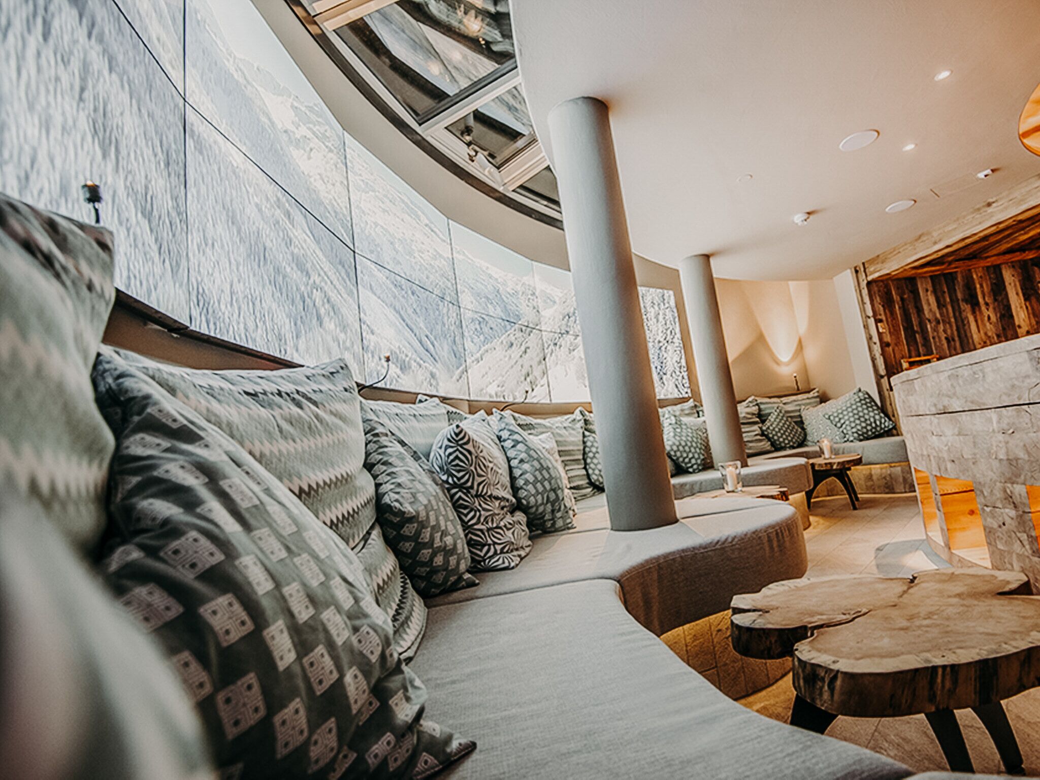 A modern interior with a curved seating area, a wooden coffee table, and a large window with a view of the mountains.