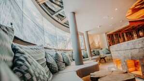 A modern lounge area with a curved seating arrangement, a fireplace, and a view of the mountains through a skylight. - Sendlhofer's (Bad Hofgastein)