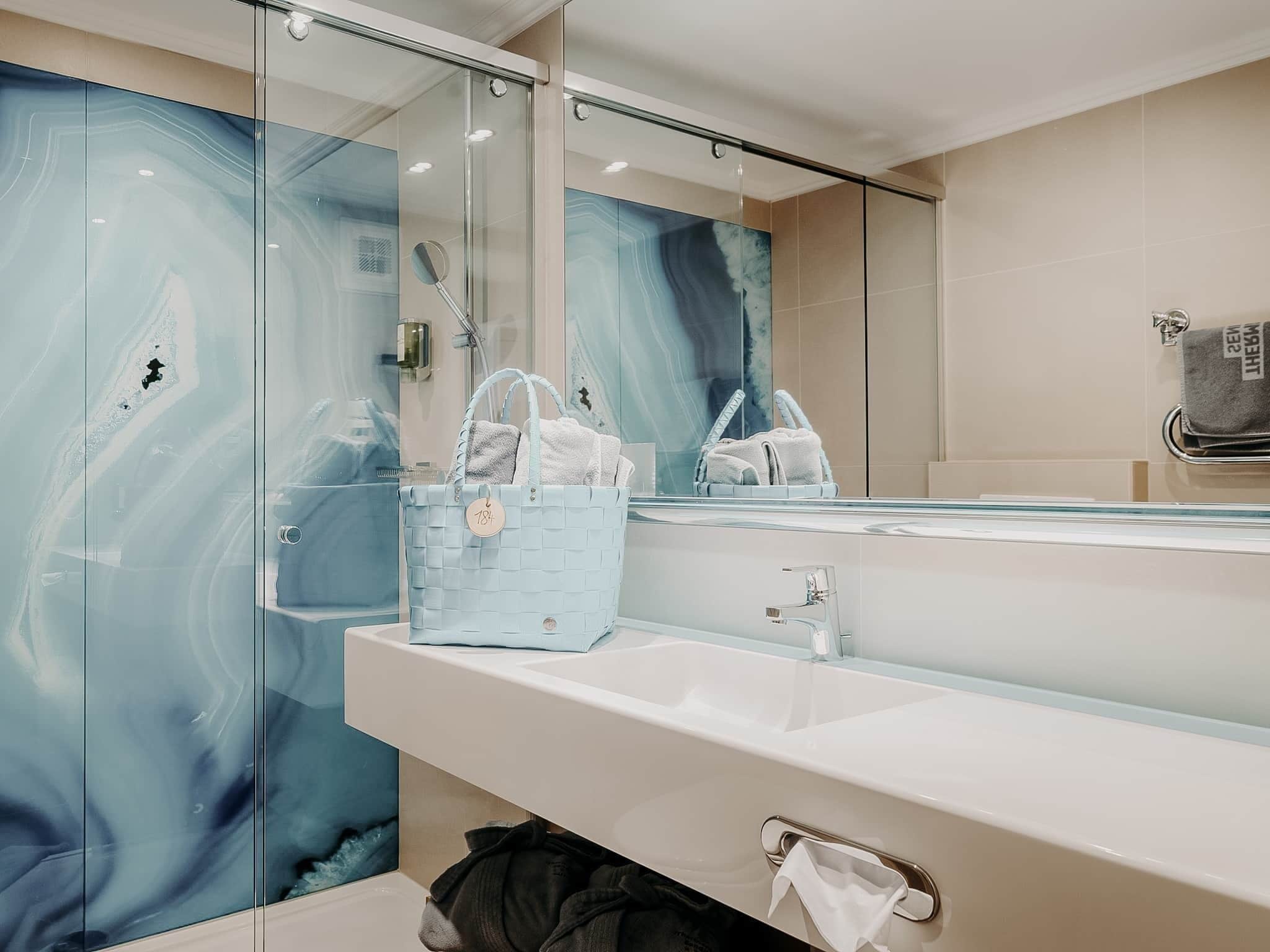 A bathroom with a glass shower enclosure, a white sink, and a large mirror.