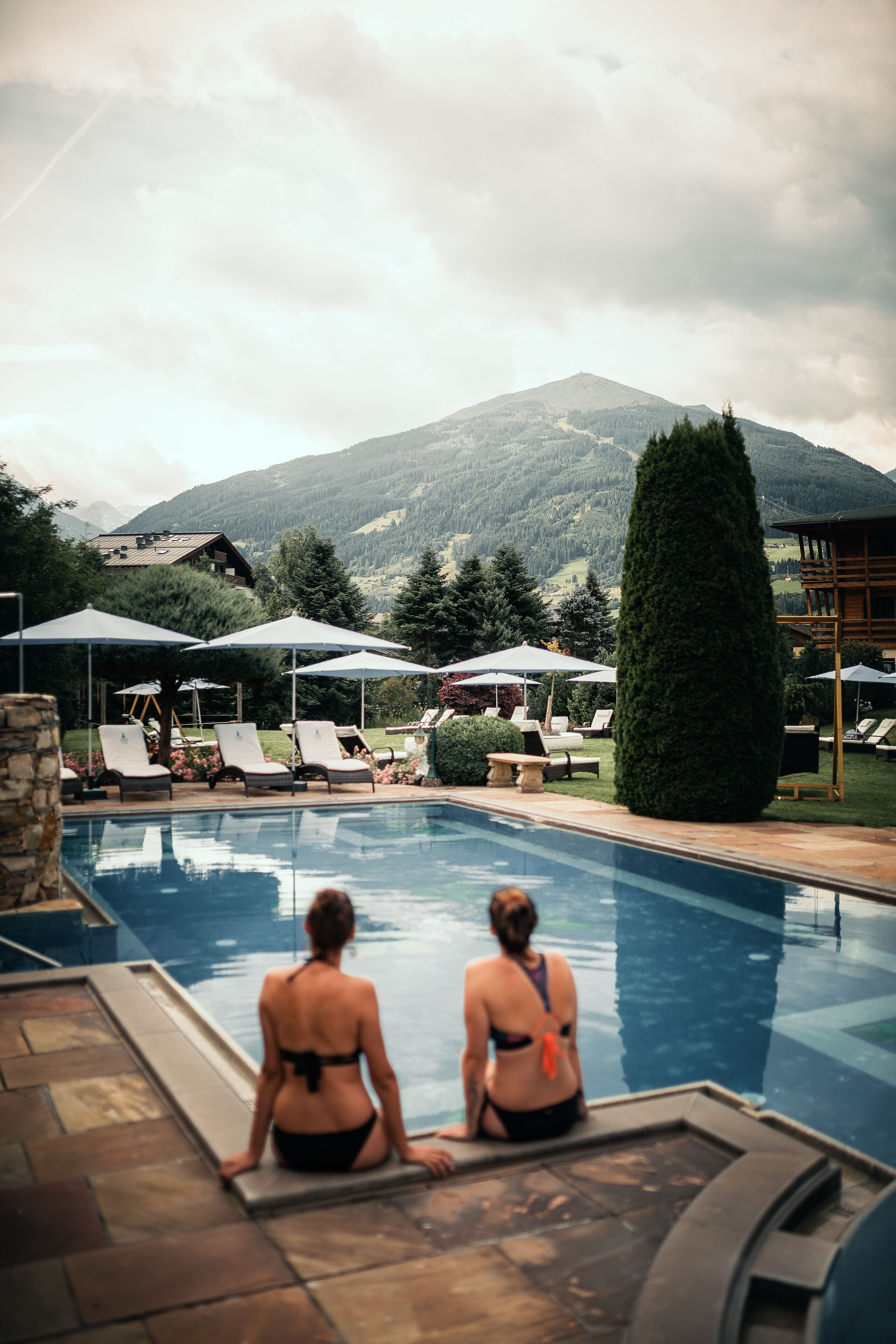 Un espace piscine agrémenté de chaises longues et de parasols, un mur en pierre et une vue sur les montagnes en arrière-plan.