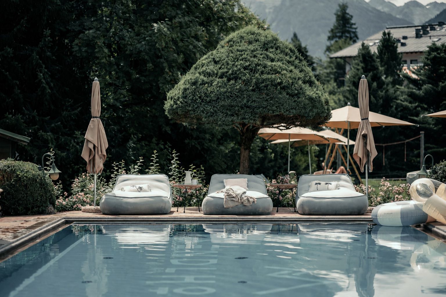 A poolside area with lounge chairs, umbrellas, and a clear view of the surrounding greenery and mountains.
