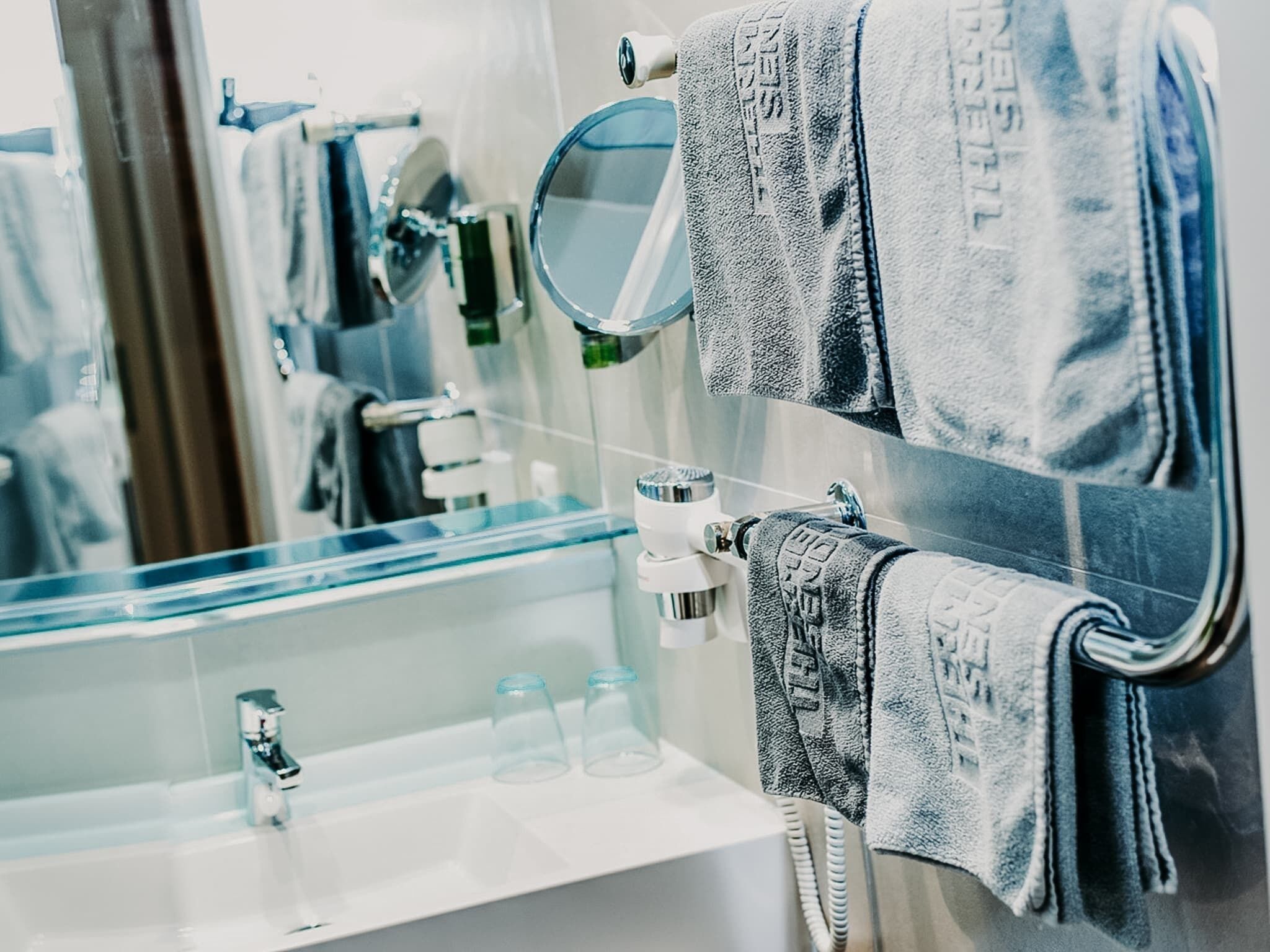 Une salle de bain avec un lavabo en verre, deux miroirs et plusieurs serviettes suspendues à un porte-serviettes.