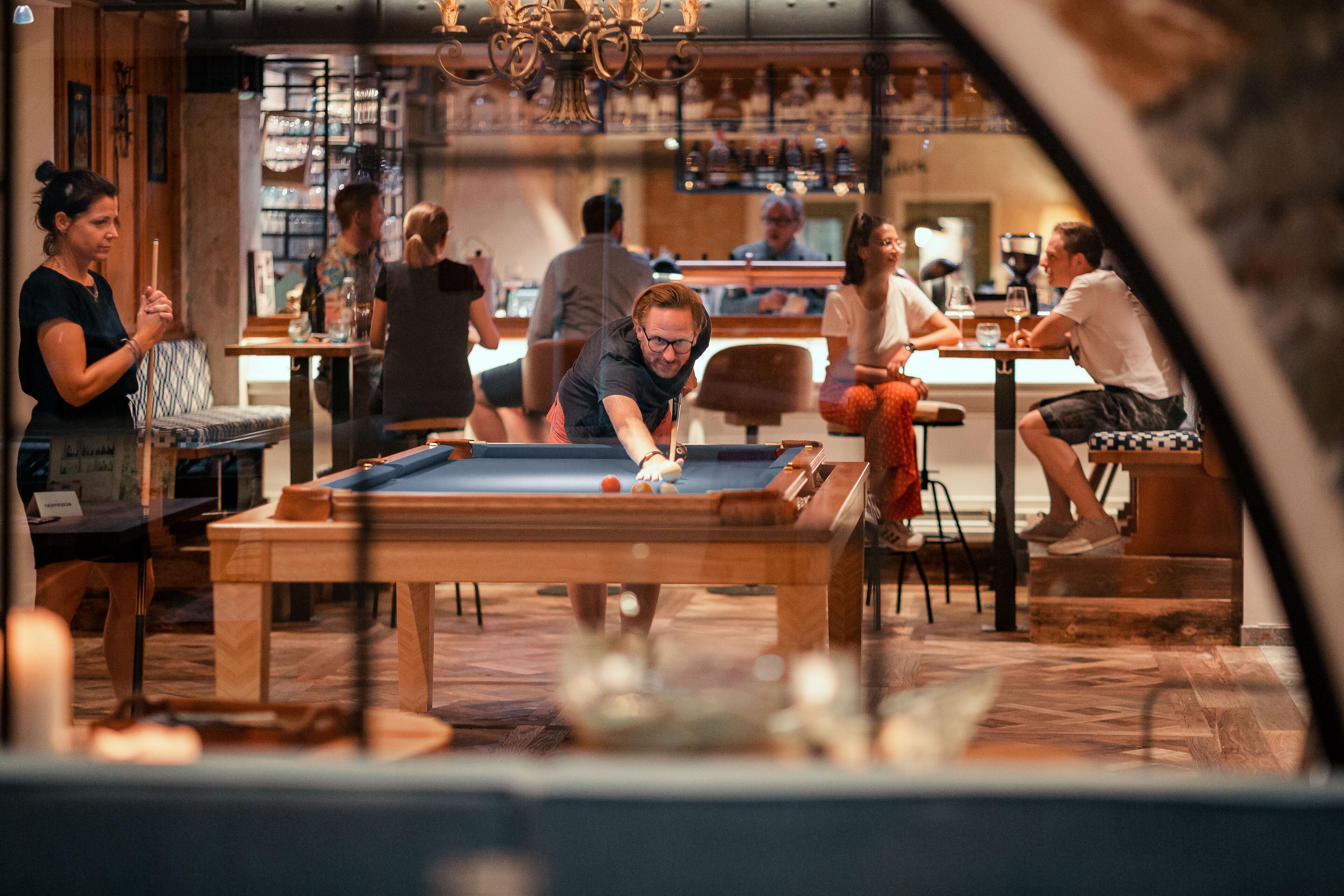 A billiards table in a bar setting with patrons around.