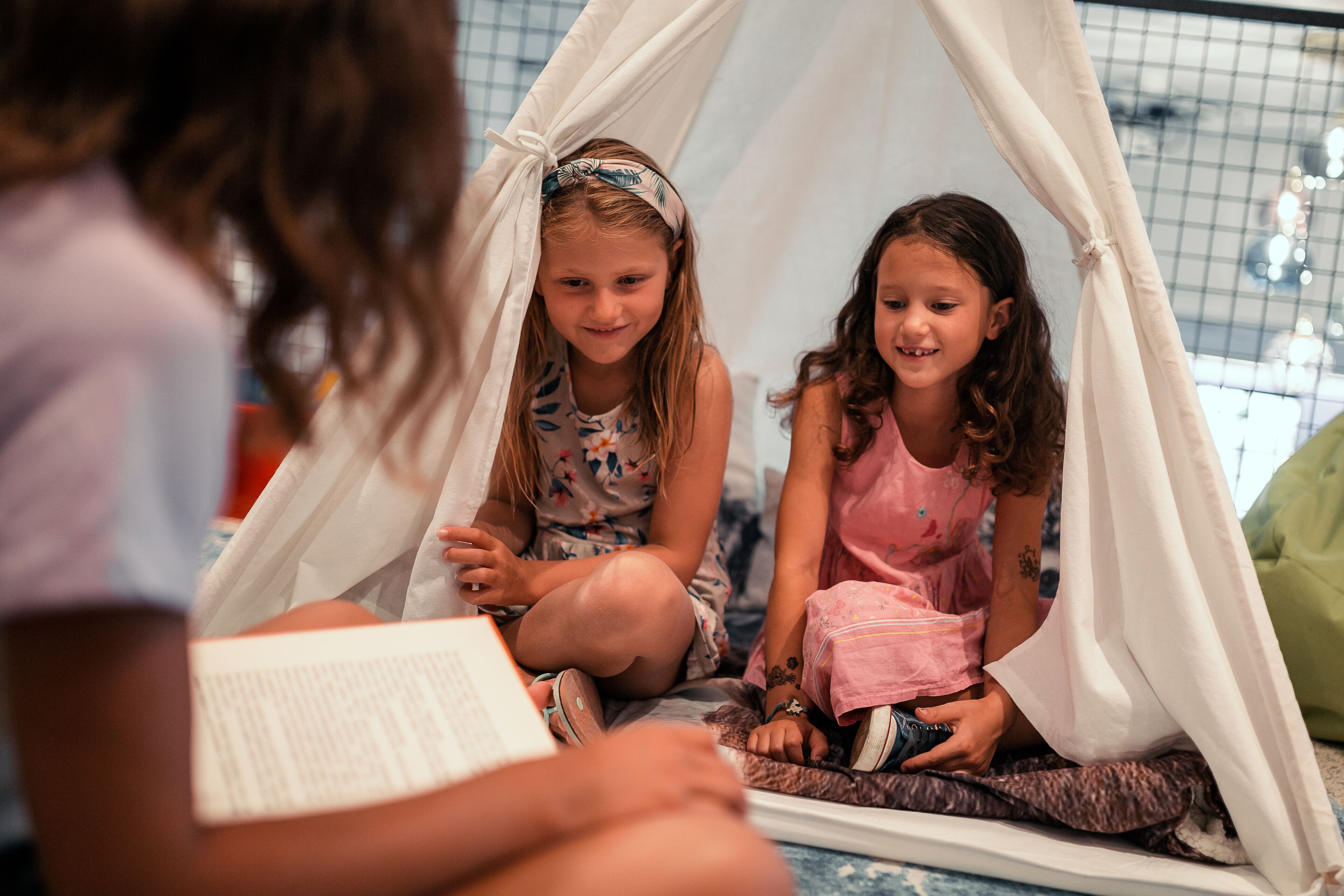 Dos niños sentados dentro de una estructura que parece una tienda de campaña, posiblemente en un área de juegos o salón de clases.
