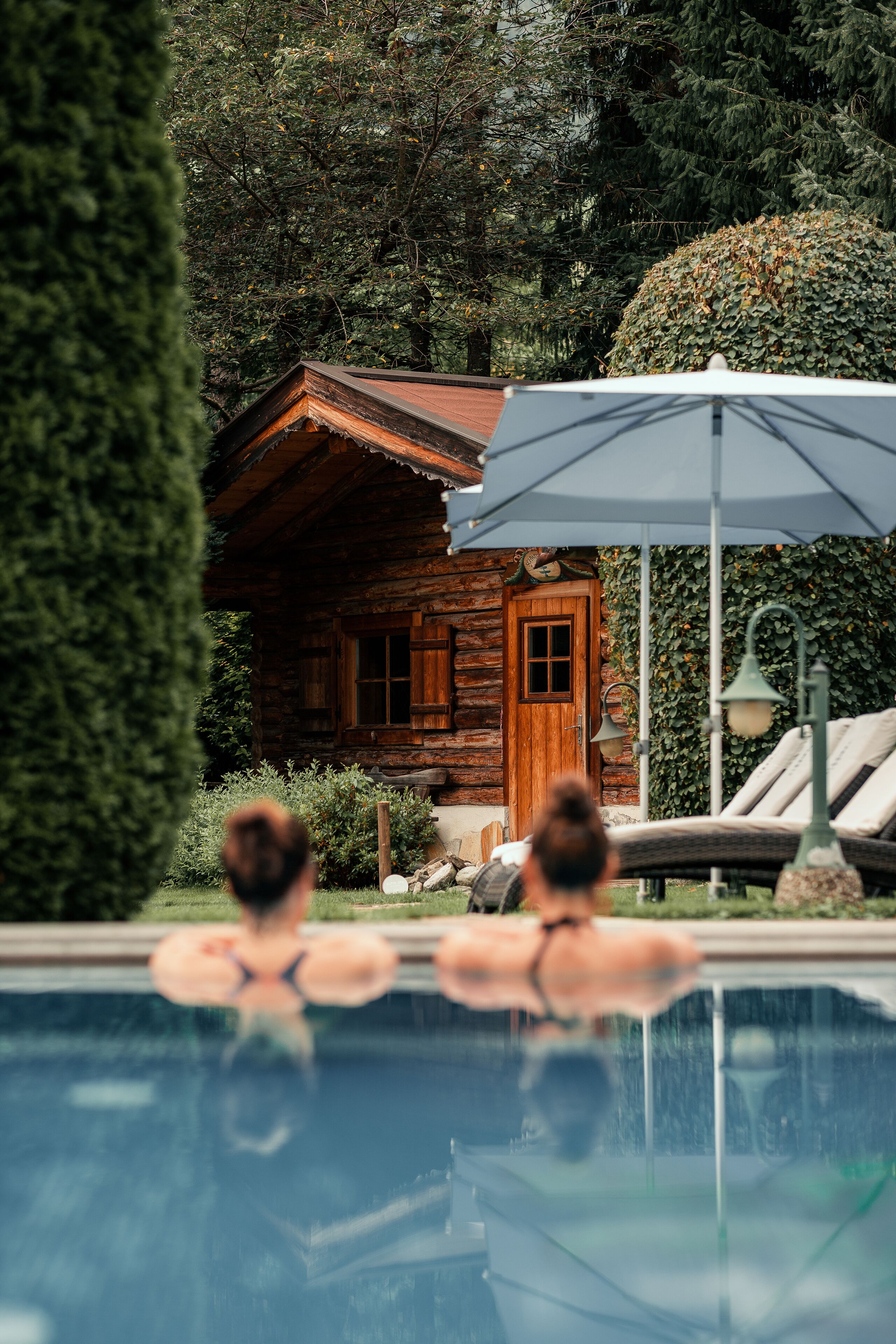 A wooden cabin with a swimming pool, surrounded by greenery.