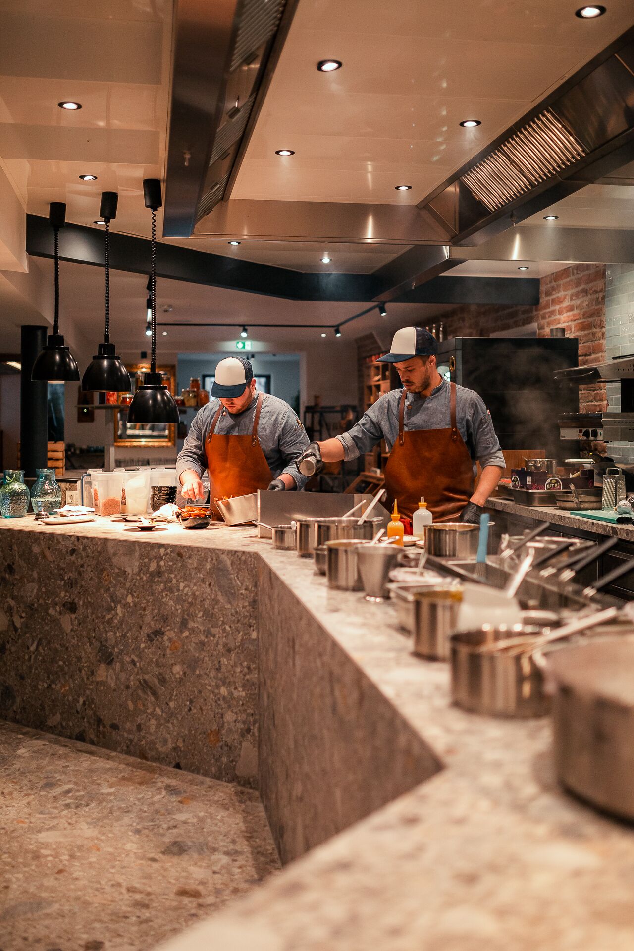Una cocina comercial con cocineros trabajando, equipada con electrodomésticos de acero inoxidable y una encimera de mármol.