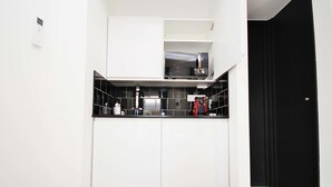 A modern kitchen with white cabinetry, black countertops, and a microwave on the upper shelf. - 6 Portobello Road (London)