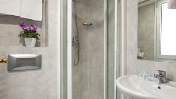 Een badkamer met een douche, wastafel en een potplant.