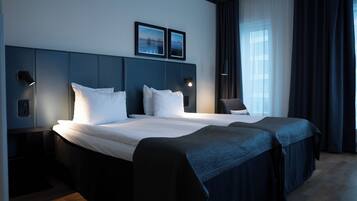A hotel room with a large bed, two bedside tables, a headboard with wall art, and a window with curtains.