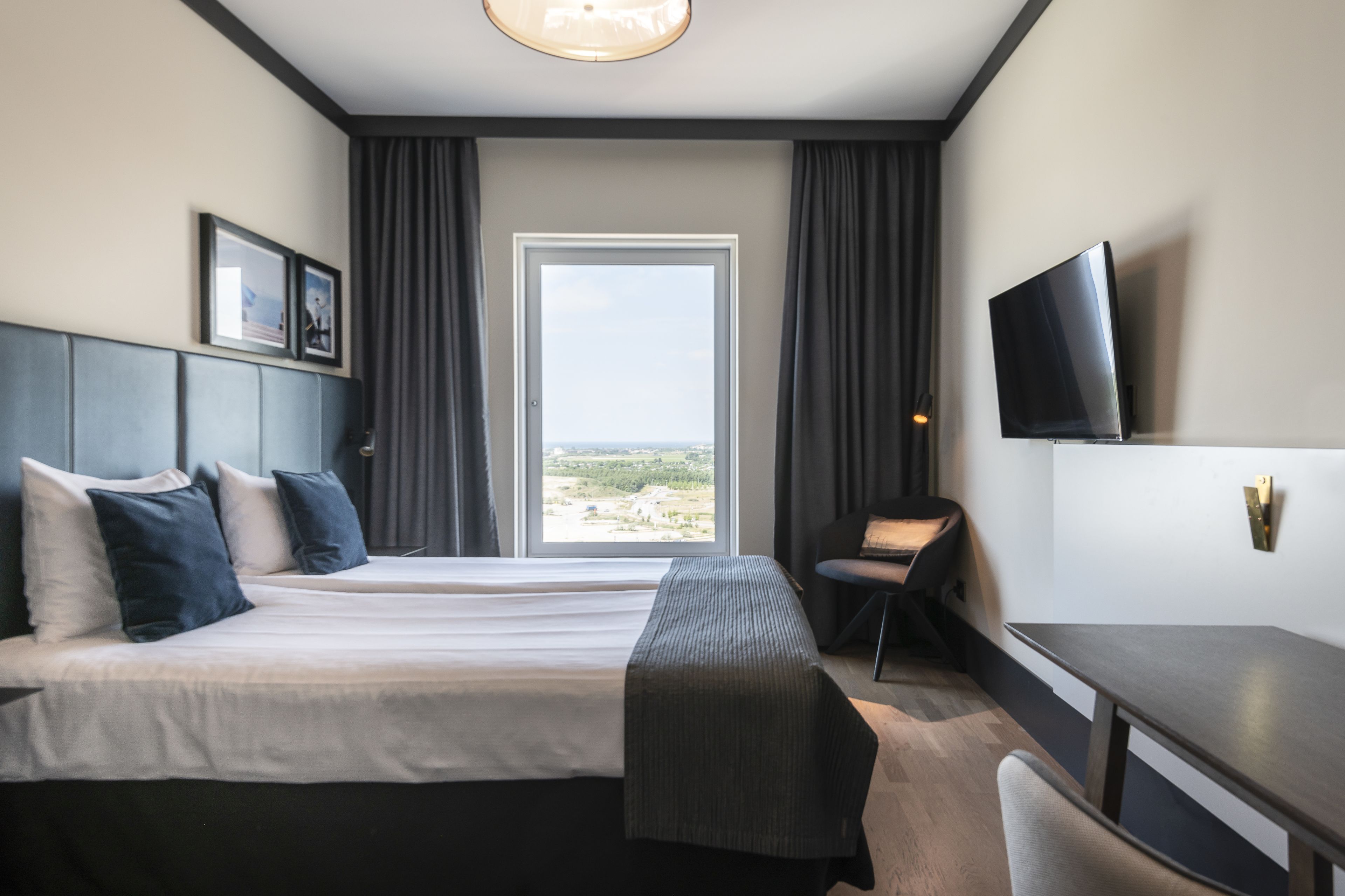 Una habitación de hotel con una cama grande, un escritorio, una silla, un televisor y una ventana con vistas al paisaje.