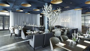 A modern restaurant with dark wood flooring, grey upholstered chairs, and tables set with white tablecloths and candles. - Quality Hotel View (Malmö)