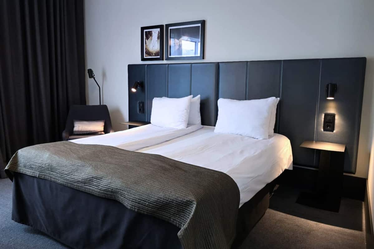 A hotel room with a large bed, two bedside tables with lamps, a chair, and two framed pictures on the wall.