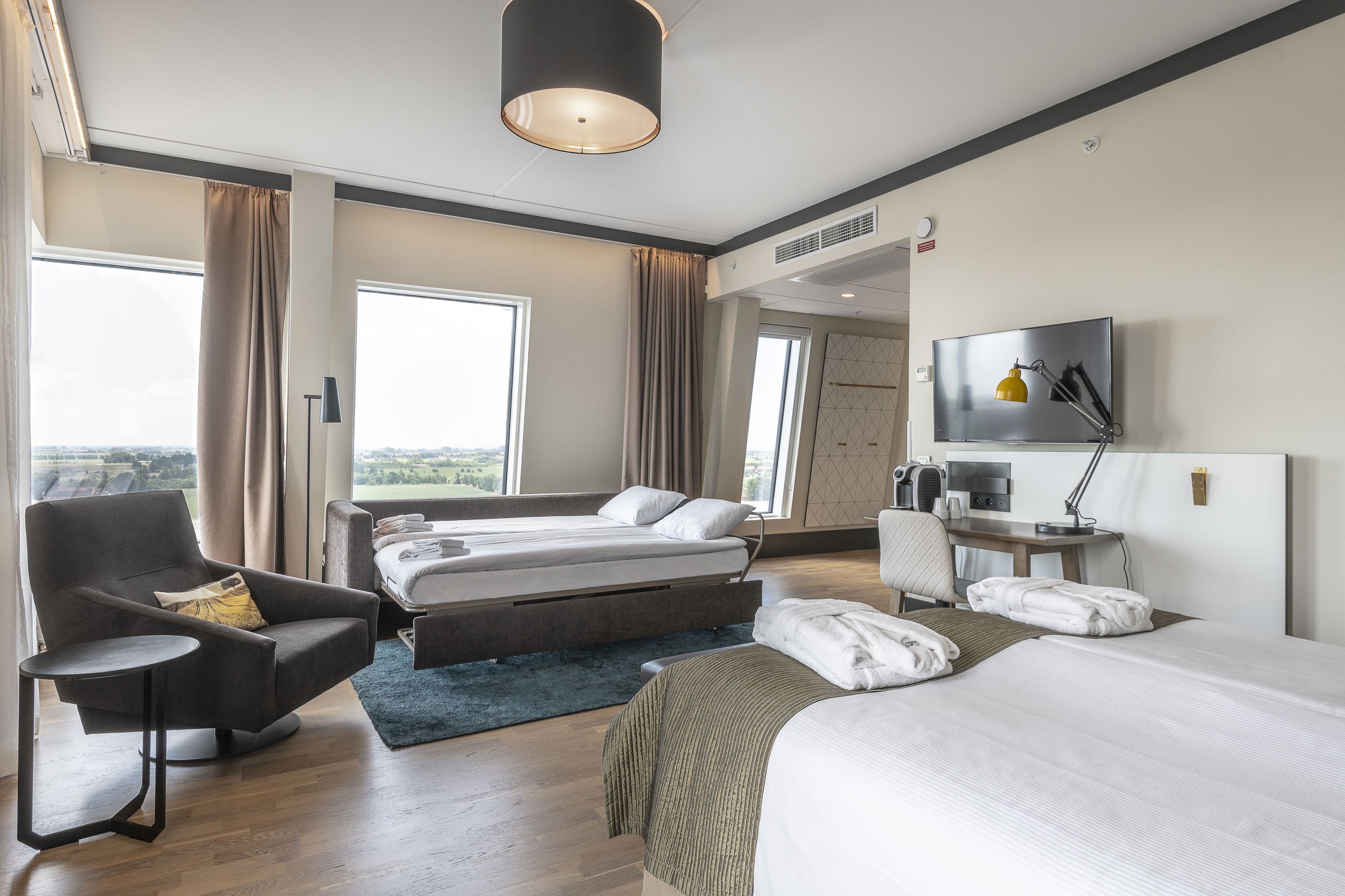 Een moderne hotelkamer met een bed, een sofa, een bureau en een televisie.