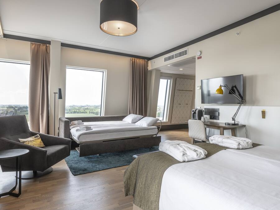 Una habitación de hotel moderna con cama, sofá, escritorio y televisor.