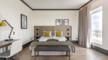 A modern hotel room with a large bed, a desk, a chair, and a view of the city.