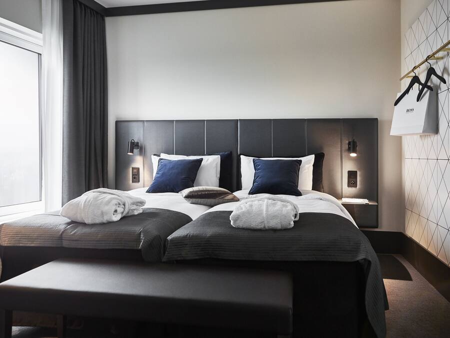 Habitación de hotel moderna con una cama grande, dos mesitas de noche, un banco y vistas al exterior.