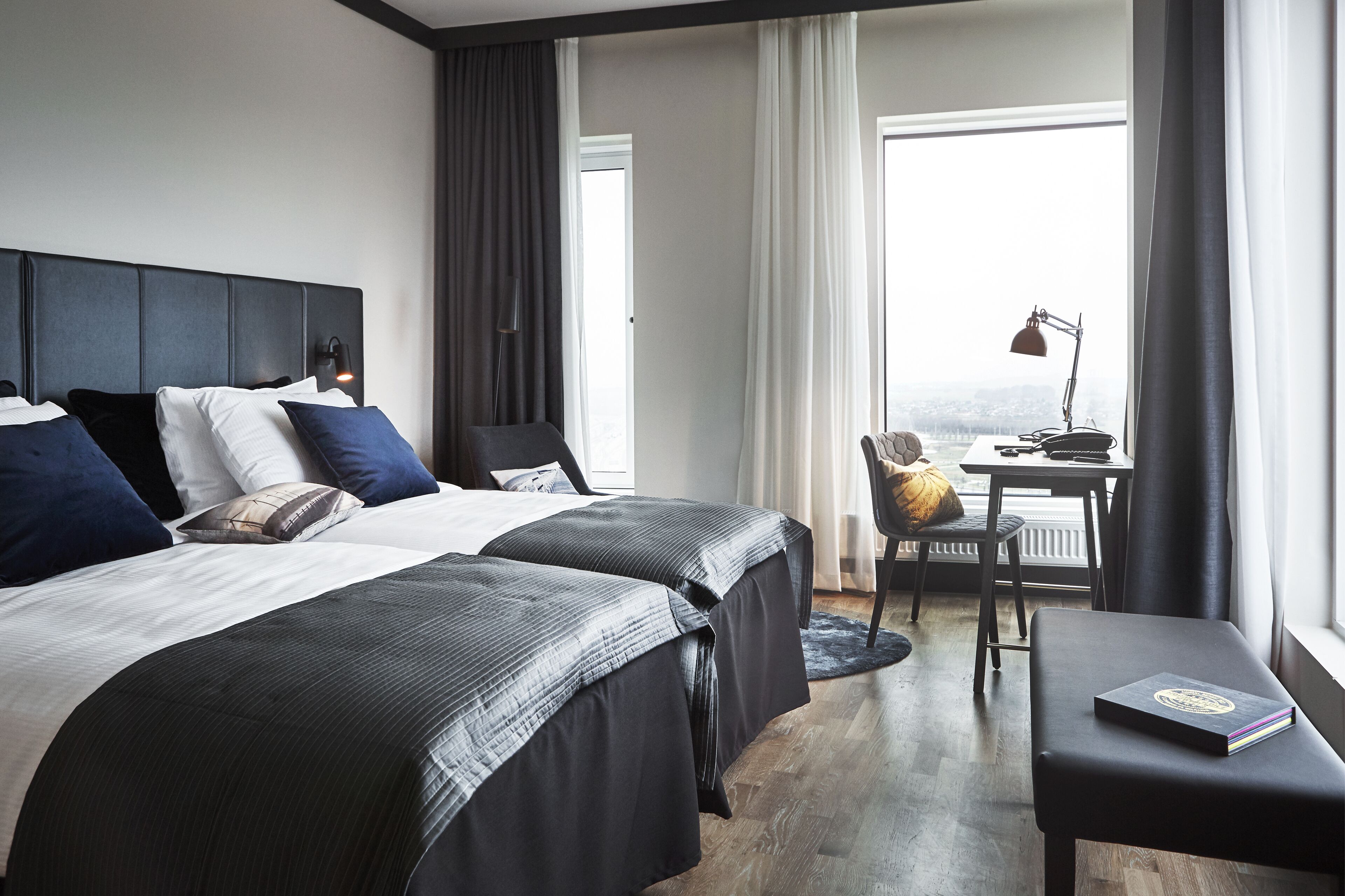 Habitación de hotel con dos camas, un escritorio, una silla y vistas a la ciudad.