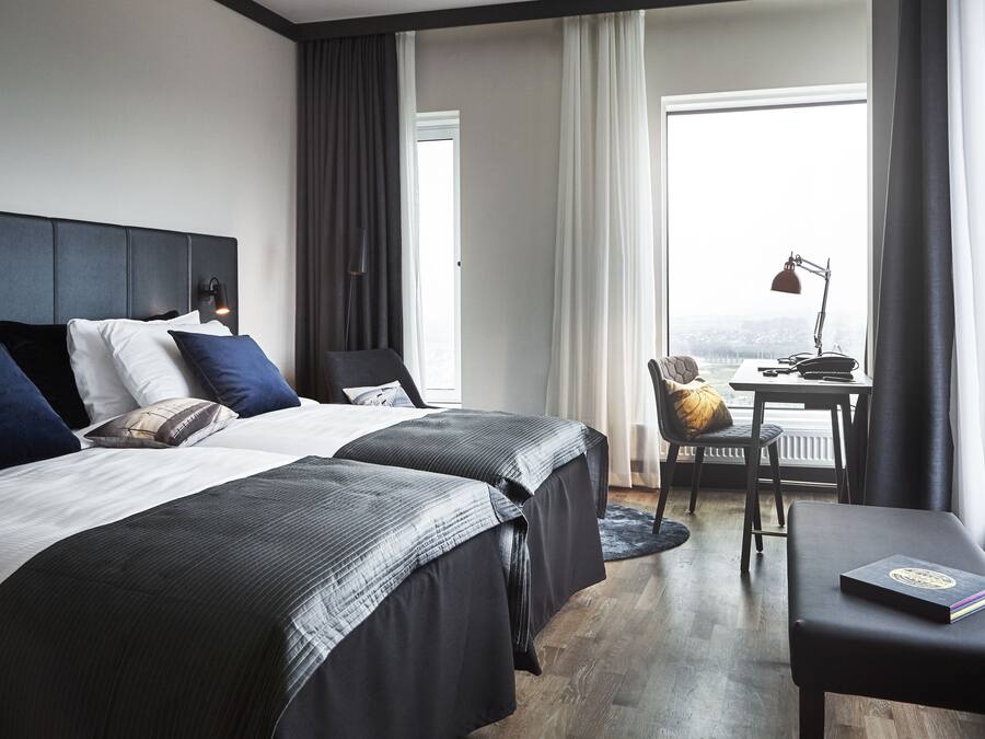 Habitación de hotel con dos camas, un escritorio, una silla y vistas a la ciudad.