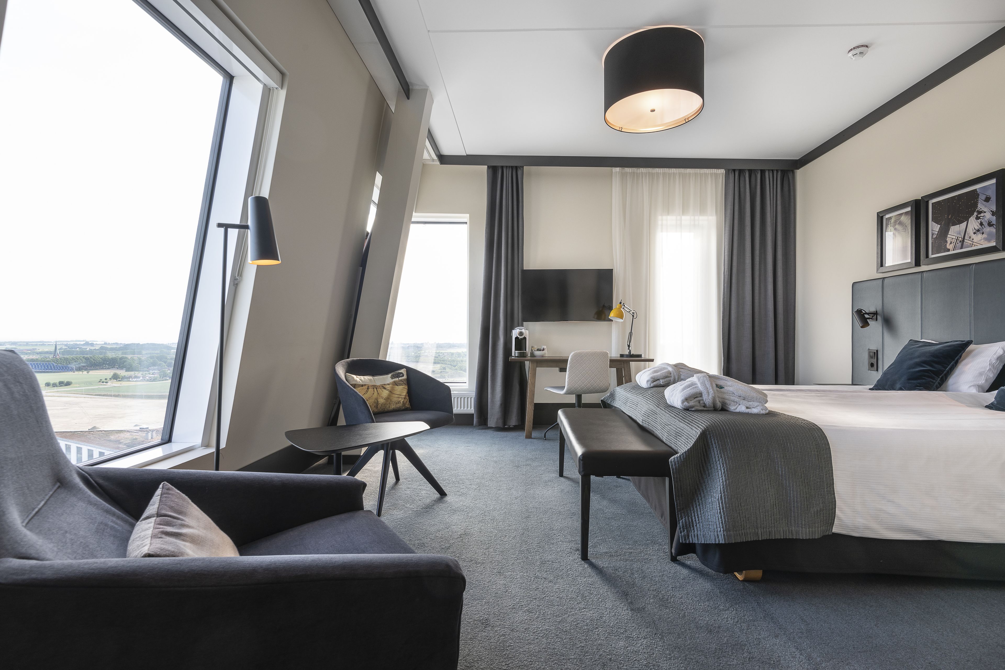 Quarto de hotel moderno com uma cama grande, uma escrivaninha, uma cadeira e um sofá.