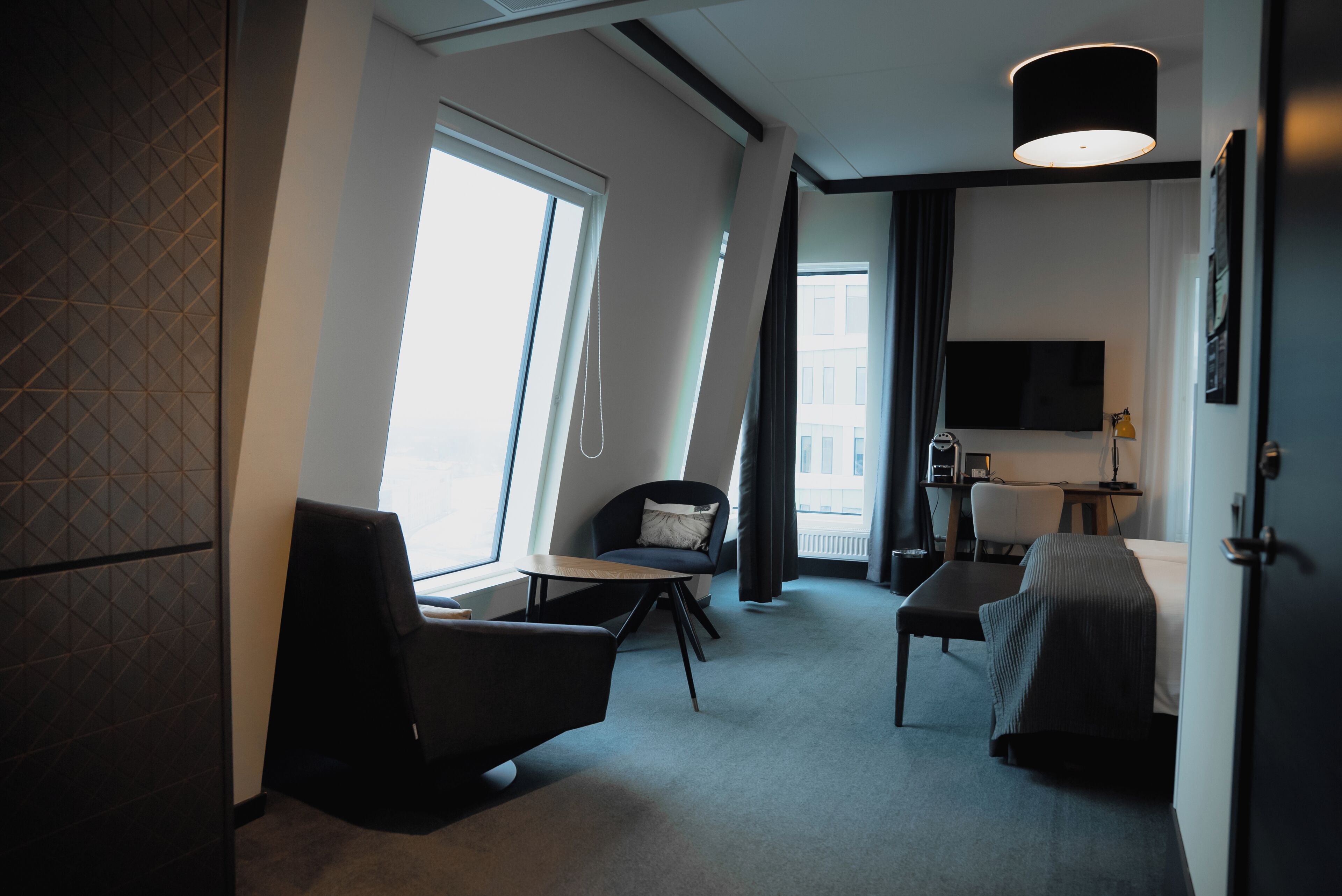 Una habitación de hotel moderna con un ventanal grande, un televisor de pantalla plana, un escritorio y una zona de estar confortable.