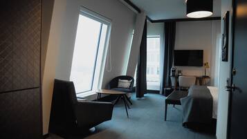 Una habitación de hotel moderna con un ventanal grande, un televisor de pantalla plana, un escritorio y una zona de estar confortable.