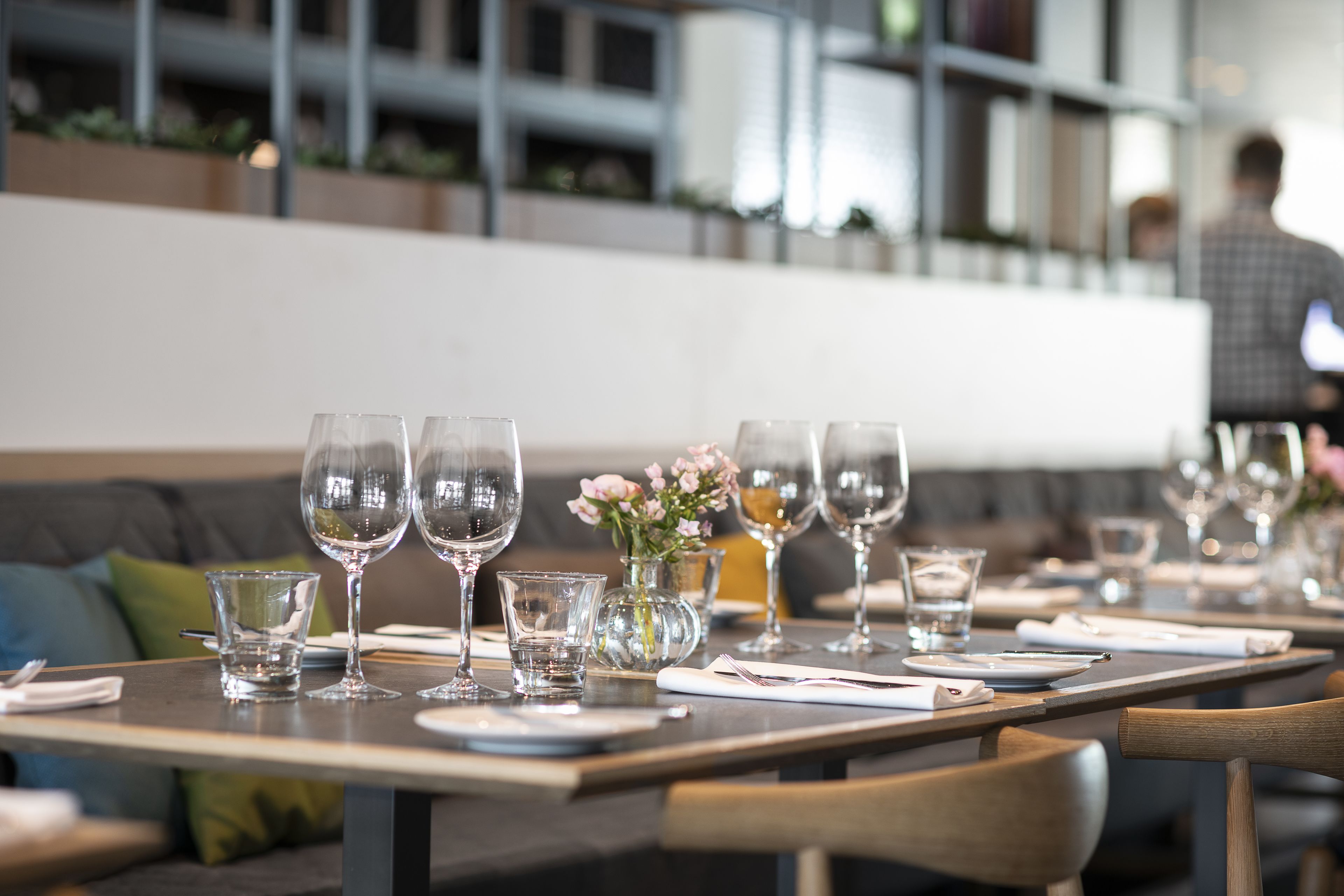 A restaurant setting with tables set for dining, featuring clear glassware and a vase with flowers.
