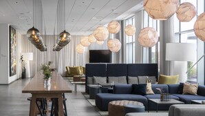 Un hall d’hôtel moderne avec une longue table en bois, des sièges confortables et de grandes fenêtres.
