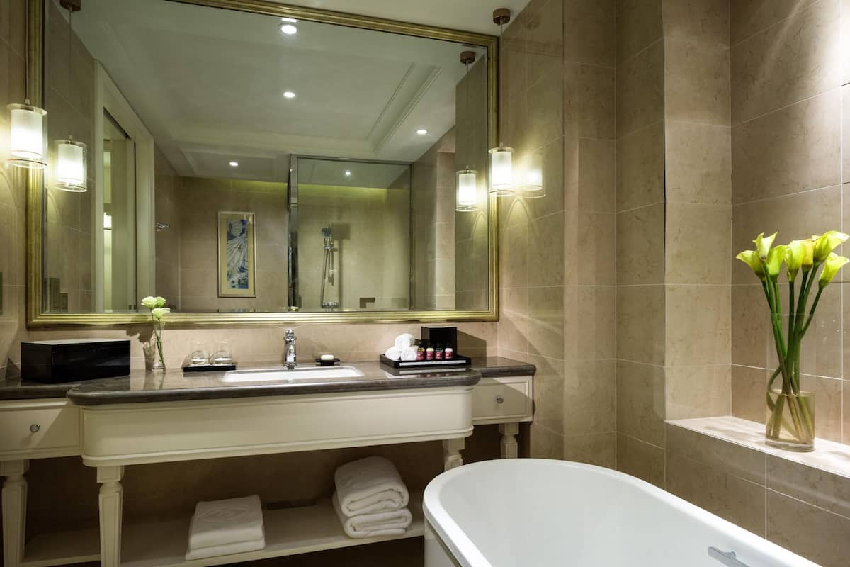 A bathroom with a large mirror, a sink, a bathtub, and a vase with flowers.