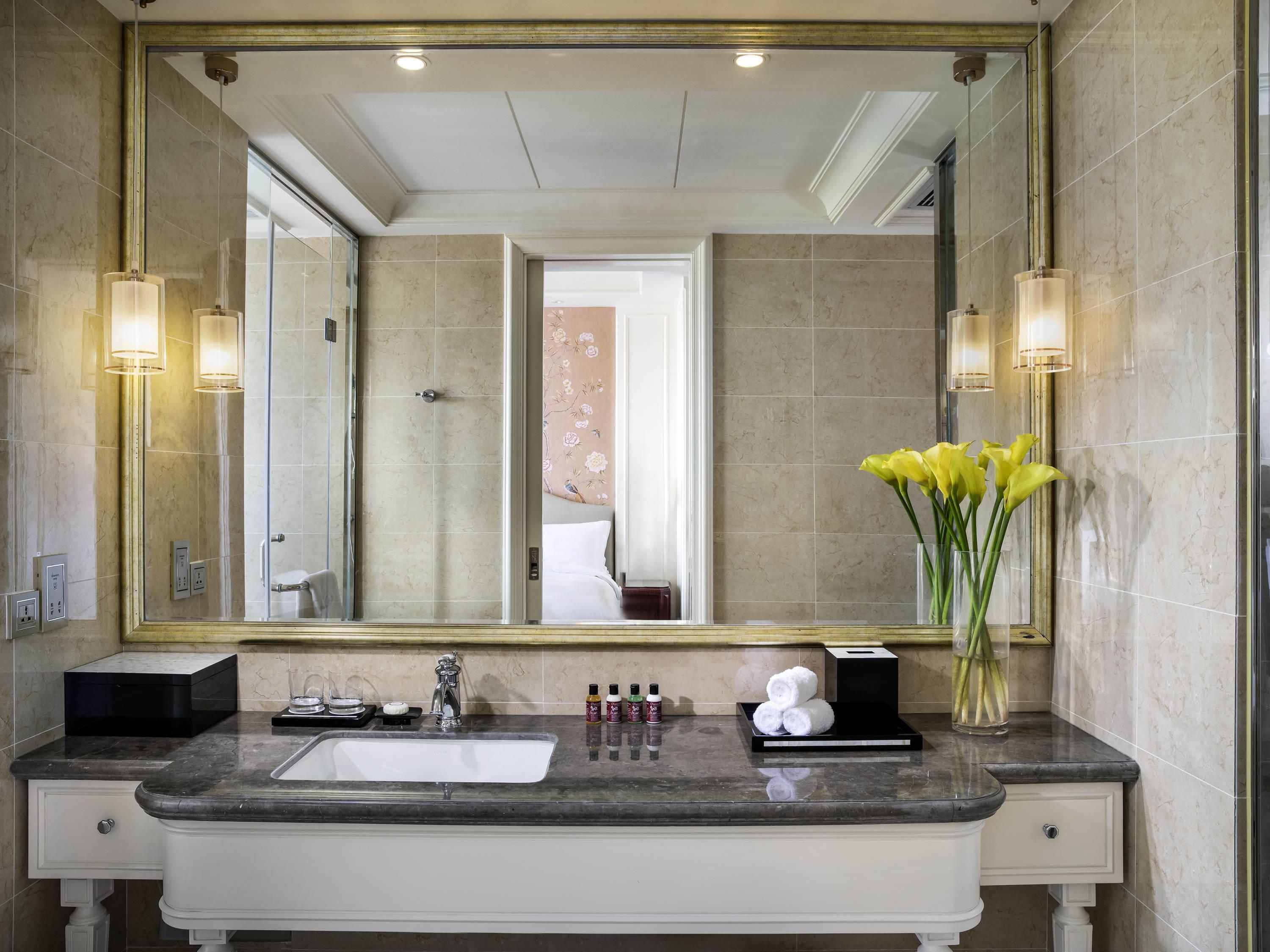 A bathroom with a large mirror, a sink, and a vase with yellow flowers.