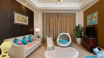 A living room with a sofa, a child’s play area, a television, and a chandelier.