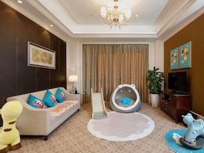 A living room with a sofa, a child’s play area, a television, and a chandelier.